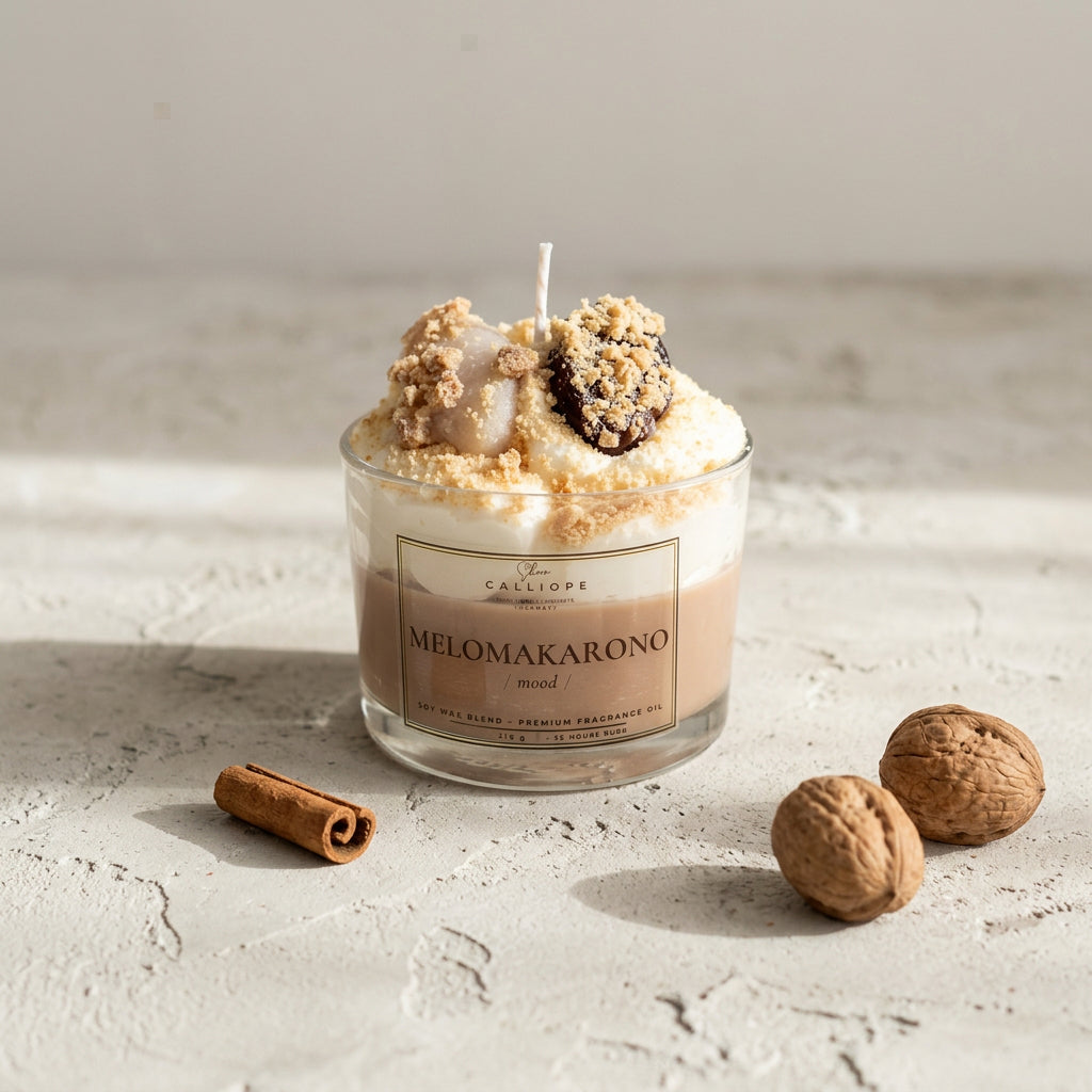 A glass jar candle with a wick and decorative toppings, labeled 'CALLIOPE MELOMAKARONO' on a light gray surface.