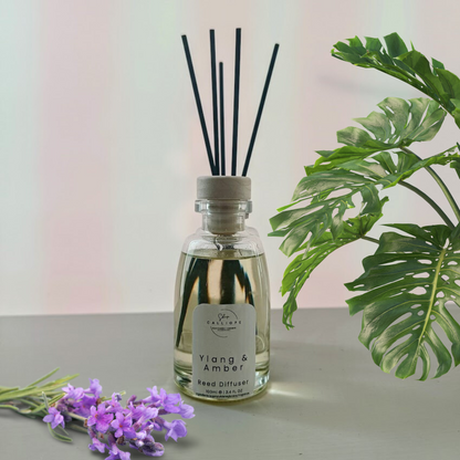 reed diffuser με άρωμα ylang & amber δίπλα σε διακοσμητικά λουλούδια
