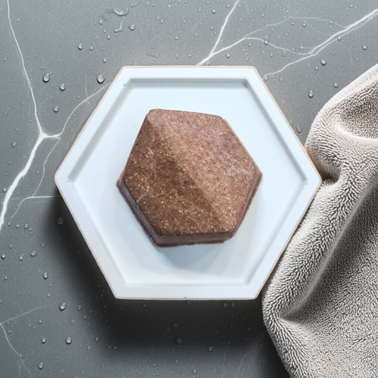 Hexagonal soap dish with a brown bar of soap on a gray surface with a towel.