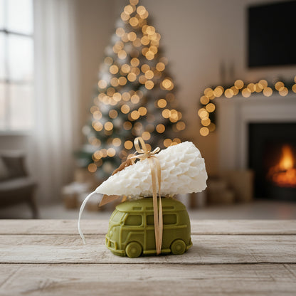 Decorative candle shaped like a van with a Christmas tree and fireplace in the background