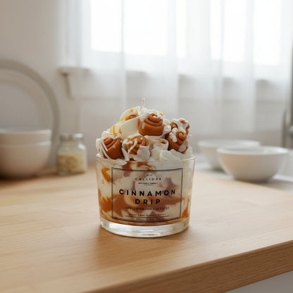 Candle labeled 'Cinnamon Drip' on a wooden surface with a blurred kitchen background