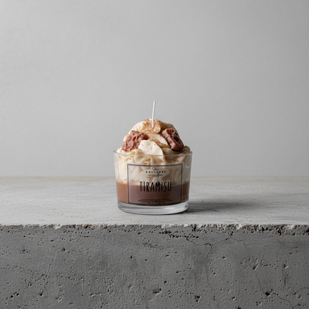 Glass container of tiramisu candle with CalliopeShop label on a concrete surface.