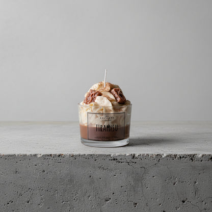 Glass container of tiramisu candle with CalliopeShop label on a concrete surface.
