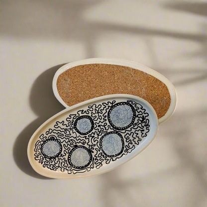 An oval, beige concrete decorative tray with cork lining, displayed with candles and decorative objects on a patterned surface.