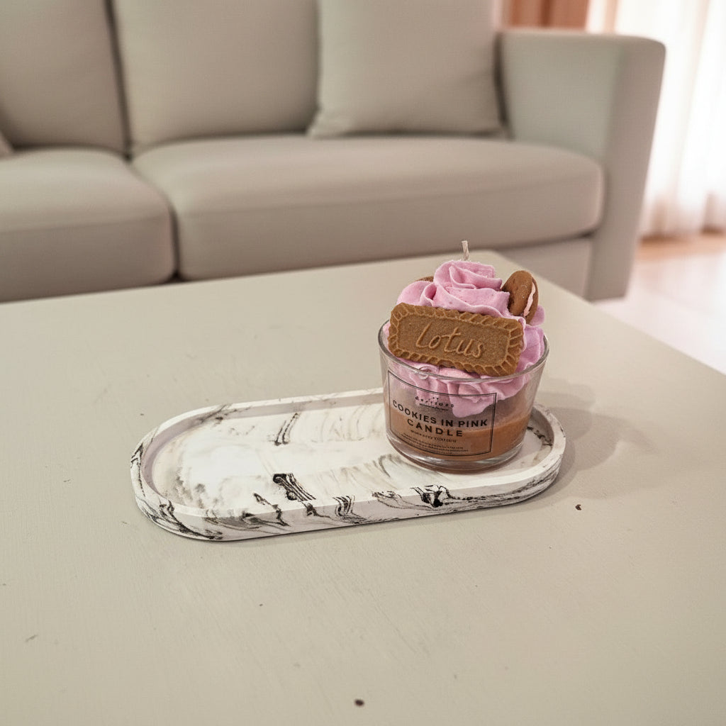 Candle with pink frosting and a cookie on top, placed on a marble tray in a living room setting.