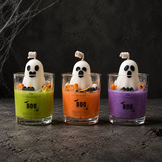 Τρία Halloween-themed αρωματικά κεριά σε ποτήρι με διακοσμητικά φαντάσματα από κερί, πάνω σε μαύρη επιφάνεια.