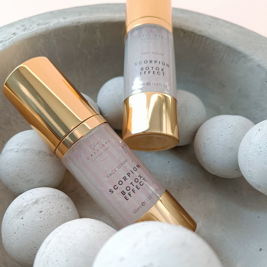 A gold-colored bottle with a pump dispenser labeled 'Scorpion Botox Effect Serum' in a cement bowl with cement beads.
