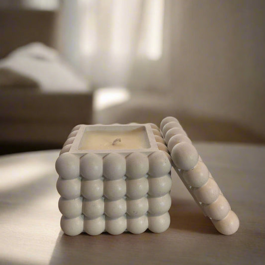 A white ceramic candle holder with a bubble design, featuring a candle inside, placed on a wooden surface with a blurred background.