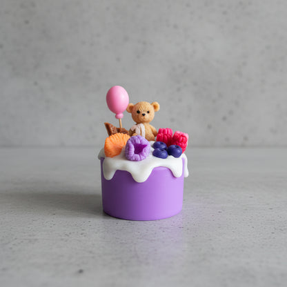 Small purple cake candle with a teddy bear, balloon, and colorful fruits on top