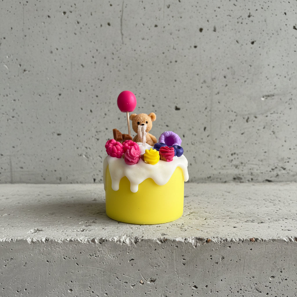 Small yellow cake candle with a teddy bear and flowers on a concrete surface