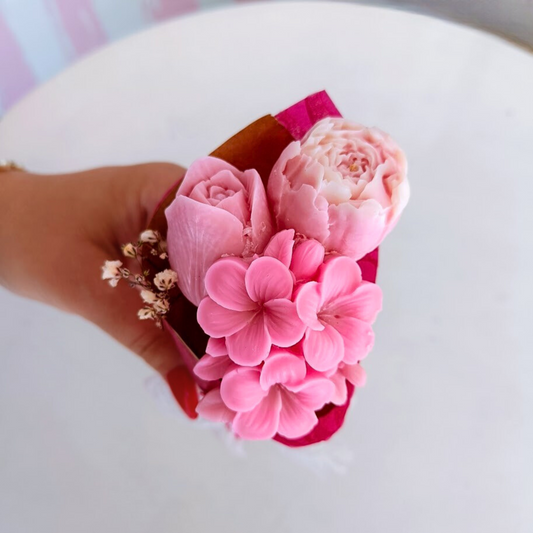 Hand holding a bouquet of pink flowers on a white surface