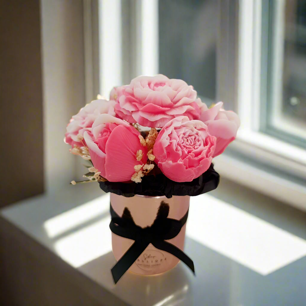Pink flower arrangement in a decorative pink container with a black ribbon on a white surface.
