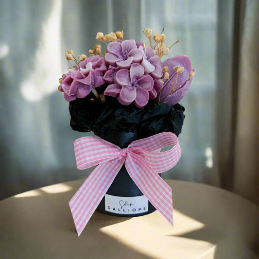Decorative flower arrangement in a black container with a pink bow on a white surface.