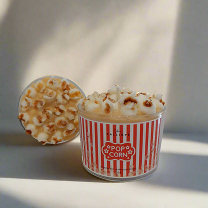 Candle in a container labeled 'Pop Corn' with popcorn design on a neutral background