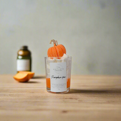 Candle shot labeled 'Pumpkin Pie' with a small pumpkin decoration on a wooden surface.