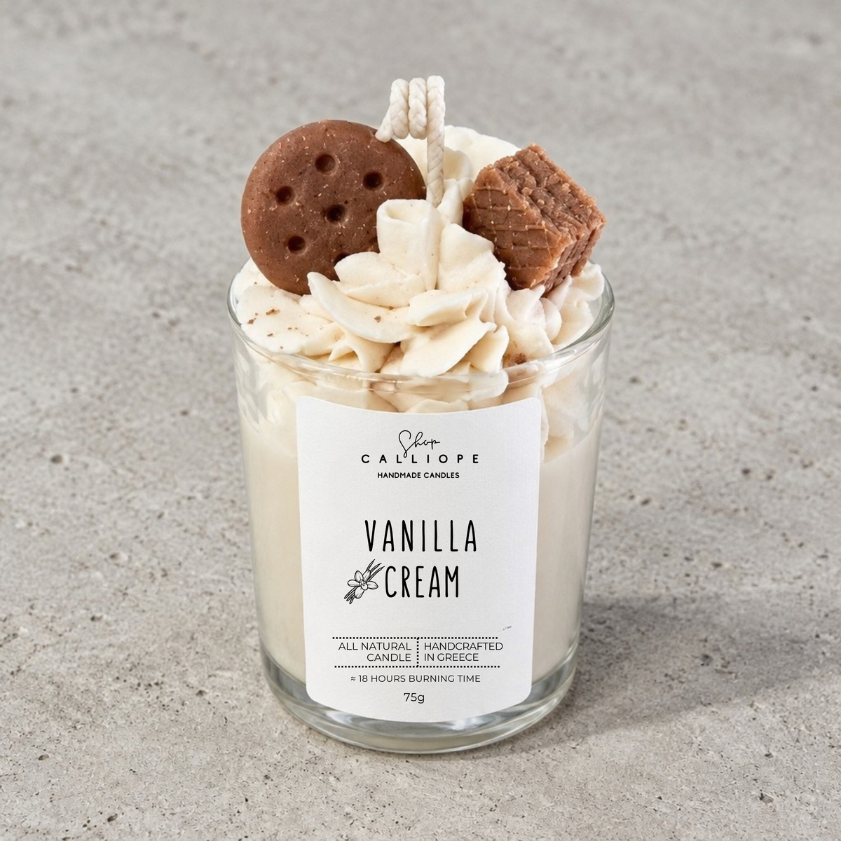 Ένα χειροποίητο κερί με άρωμα vanilla cream από την Calliope σε διάφανο γυάλινο βάζο, γαρνιρισμένο με σαντιγί, ένα μπισκότο γεμιστό και ένα κομμάτι βάφλας, τοποθετημένο σε ένα ανάγλυφο γκρι φόντο.