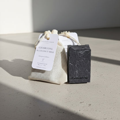 Bar of charcoal soap with a drawstring bag labeled 'Charcoal & Coconut Milk' on a concrete surface.