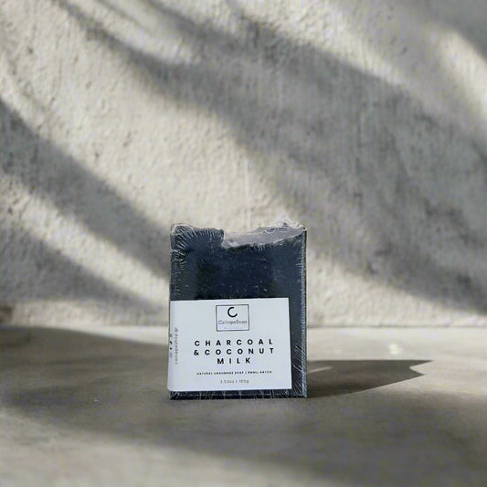 Bar of charcoal and coconut milk soap in packaging on a light gray background