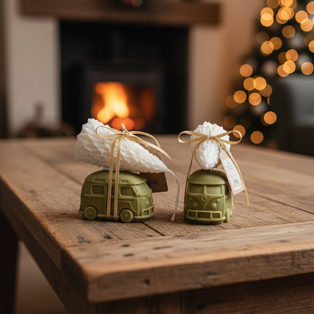 Two green toy cars with white wreaths on a wooden table in front of a fireplace and Christmas tree.