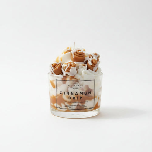 Candle labeled 'Cinnamon Drip' on a wooden surface with a blurred kitchen background