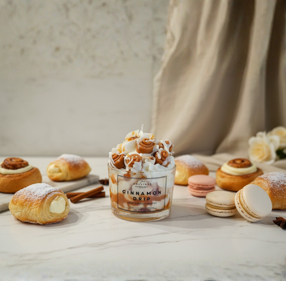 Candle with cinnamon flavor surrounded by pastries on a marble counter.