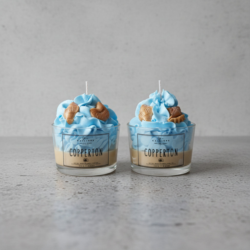 Two blue-themed candles with shell figures in glass containers on a concrete surface.
