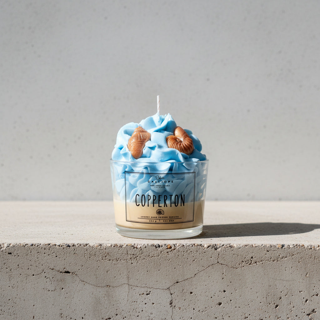 Candle in a container labeled 'Copperton' with blue wax and shell decorations.