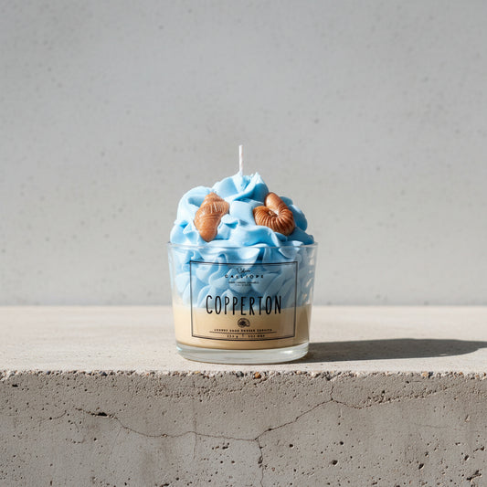 Candle in a container labeled 'Copperton' with blue wax and shell decorations.