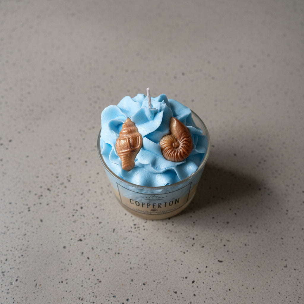 Candle in a glass container with blue wax and conch shell decorations, branded 'Copperton'.