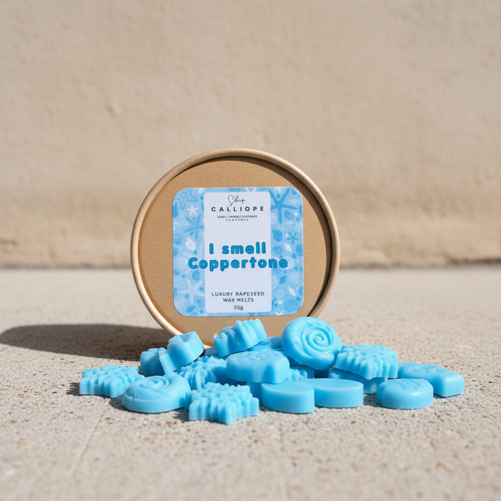 Μπλε ψαράκια και κοχύλια wax melts πάνω σε πέτρινη επιφάνεια μπροστά από κραφτ στρογγυλό κουτί με ετικέτα i smell coppertone CalliopeShop