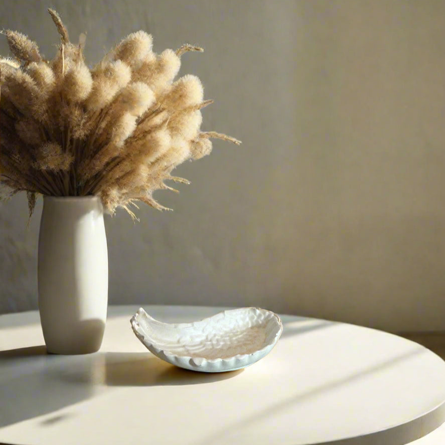 Διακοσμητικός δίσκος σε σχήμα φτερού πάνω σε λευκή επιφάνεια δίπλα απο λουλούδια