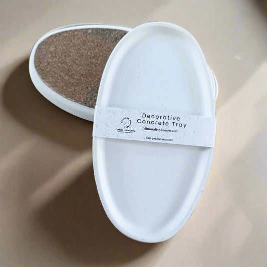 An oval, beige concrete decorative tray with cork lining, displayed with candles and decorative objects on a patterned surface.