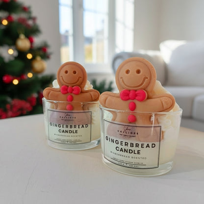 Two gingerbread candle holders with smiling faces on a surface with a Christmas tree in the background.