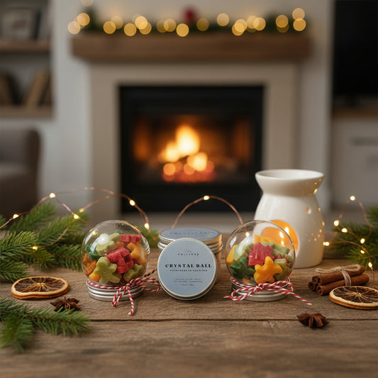 Decorative candles with festive elements on a wooden table in front of a fireplace.