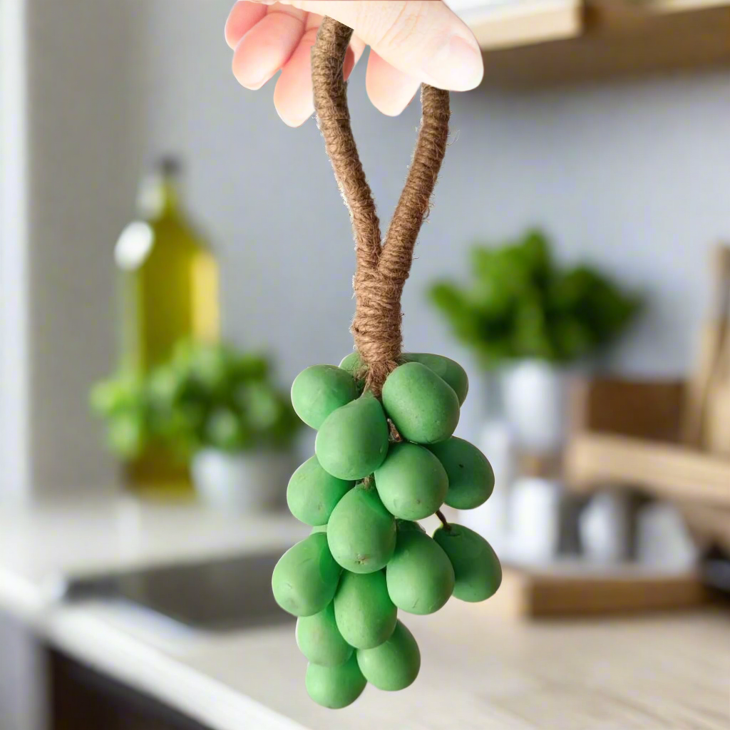 Green grape decoration with brown stem held by a hand against a neutral background
