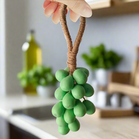 Green grape decoration with brown stem held by a hand against a neutral background