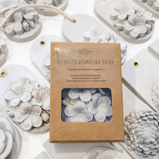 A package of handmade gypsum home fragrance shaped like white flowers, shown in its brown kraft paper box with a clear window, surrounded by several finished white flower gypsum aromatic tablets on a white background.