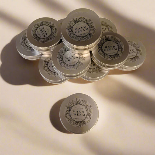 A collection of small, round metal containers with lids, branded as hand cream, displayed on a light surface with a shadow falling over part of the image.