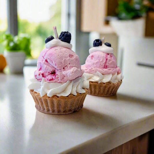 Two ice cream cups with pink scoops and whipped cream on a kitchen counter.