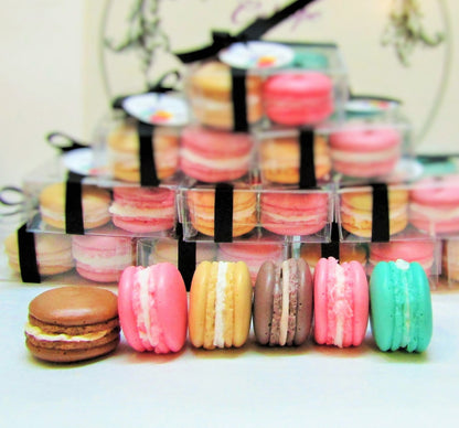 A set of four handmade 3D macaron soaps in a clear box, with each macaron featuring a different color and flavor, such as chocolate, strawberry, salted caramel, and apple.