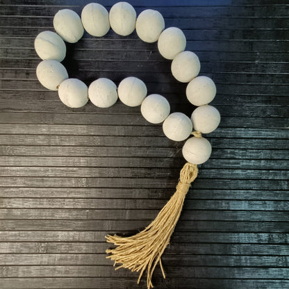 A decorative concrete komboloi with white beads and a hemp twine tassel.