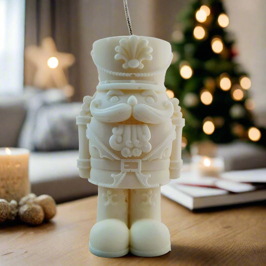 Decorative nutcracker candle ornament on a table with a blurred Christmas tree in the background.