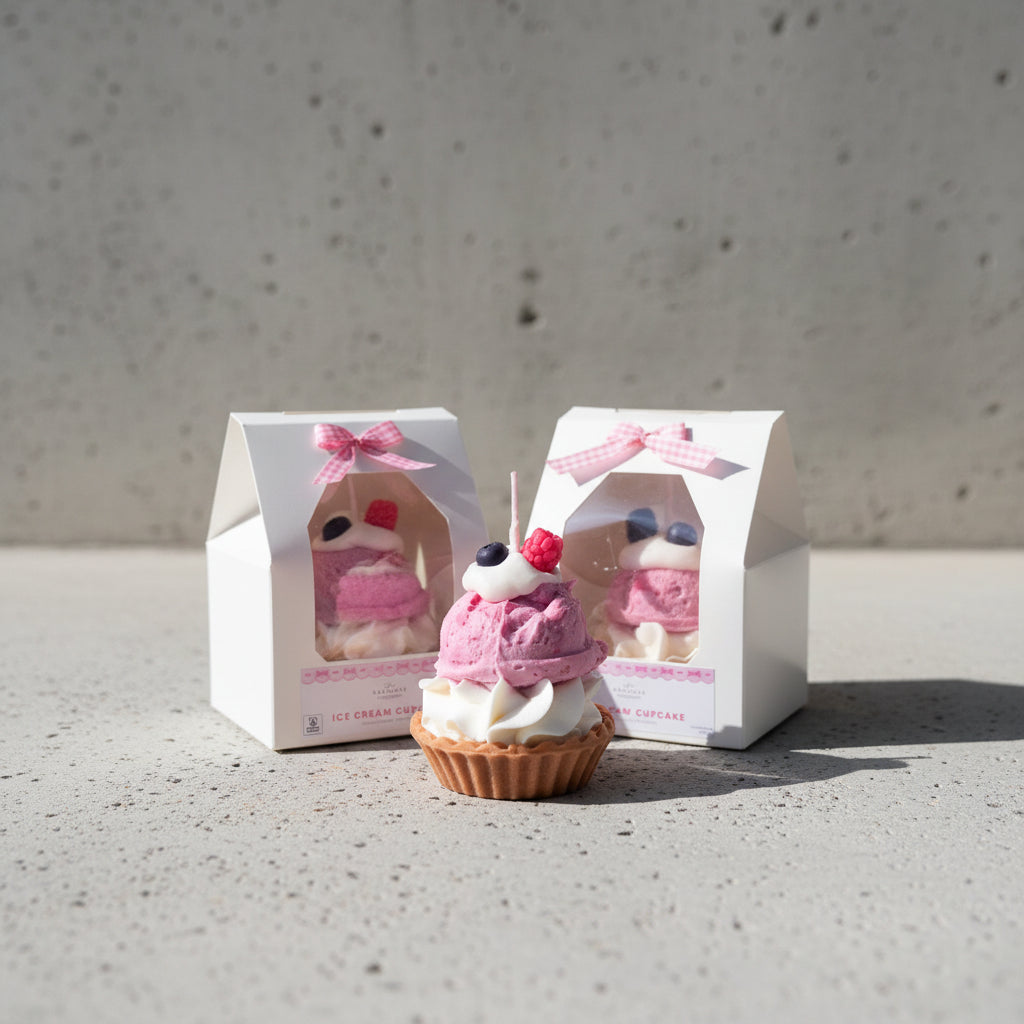 Cupcake candle with pink frosting and berries on top, displayed in front of its packaging.