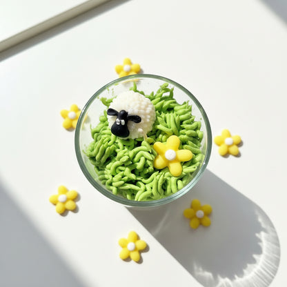 Candle Grass with a sheep and flower decoration in a glass .