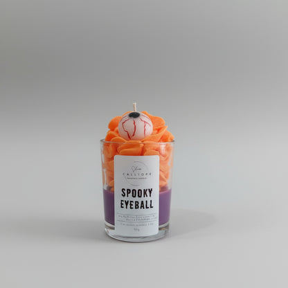 Candle labeled 'Spooky Eyeball' with decorative elements on a white surface.