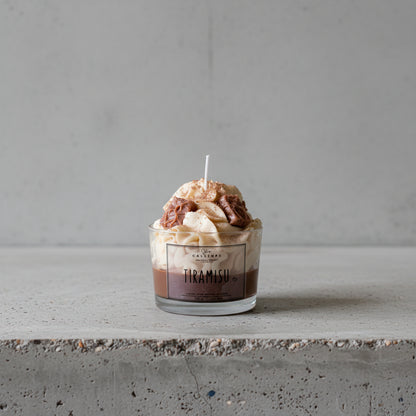 Tiramisu dessert candle in a glass container on a concrete surface.