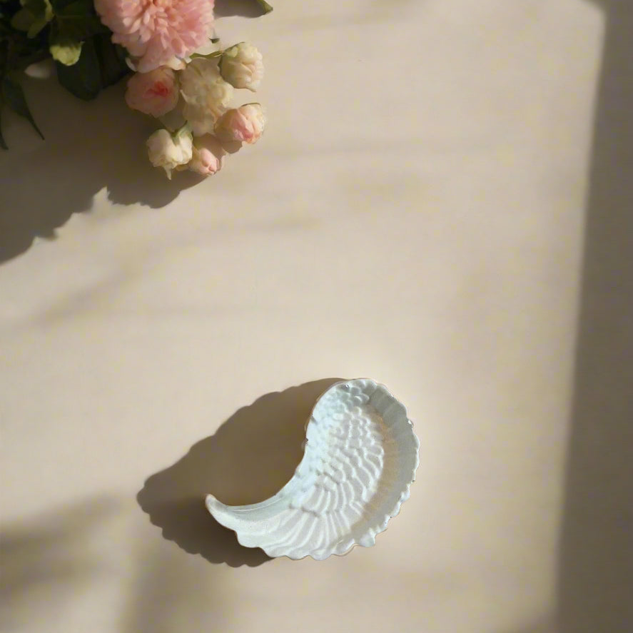 Άσπρος διακοσμητικός δίσκος με σχήμα φτερού σε φωτεινή επιφάνει με λεπτομέρειες λουλουδιών