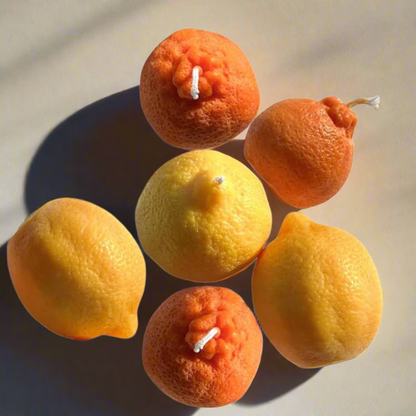 A collection of handcrafted candles designed to look like citrus fruits, specifically lemon and orange, with realistic details and a white wick.