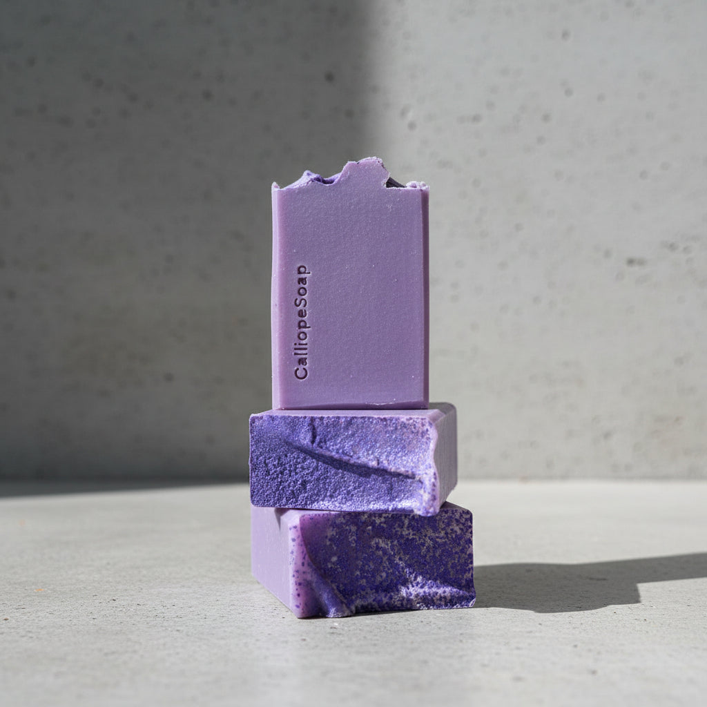 Three purple bars of soap stacked on a grey surface with a blurred background