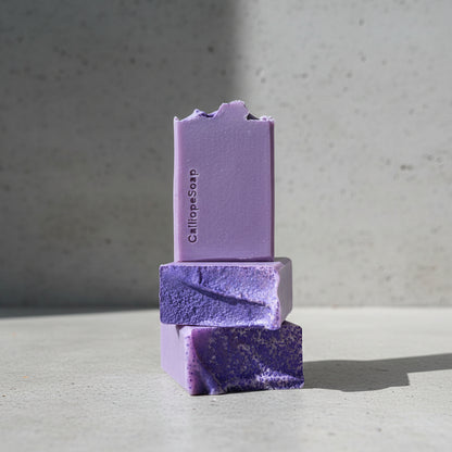 Three purple bars of soap stacked on a grey surface with a blurred background